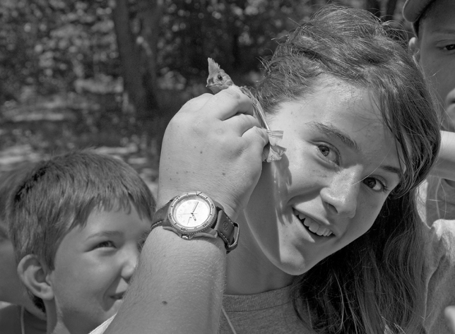 Girl listens to the heartbeat of bird with a naturalist/educator